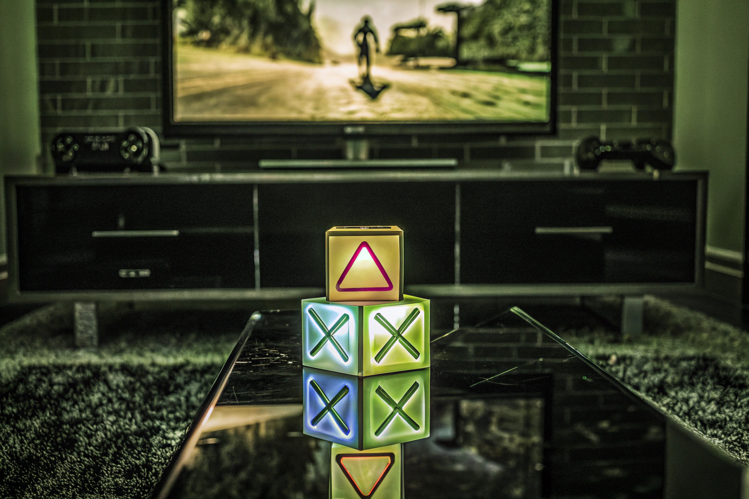 Die PlayStation Icons Leuchte, die auf einem Regal in einem Gaming-Zimmer steht und in verschiedenen Farben leuchtet. PlayStation Icons Leuchte in einem Gaming-Zimmer