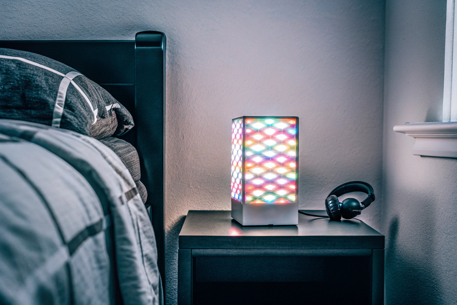 Ein moderner 3D LED Digitalwecker, der auf einem Nachttisch in einem Schlafzimmer steht und in leuchtenden Farben erstrahlt. Seutgjie 3D LED Digitalwecker auf einem Nachttisch