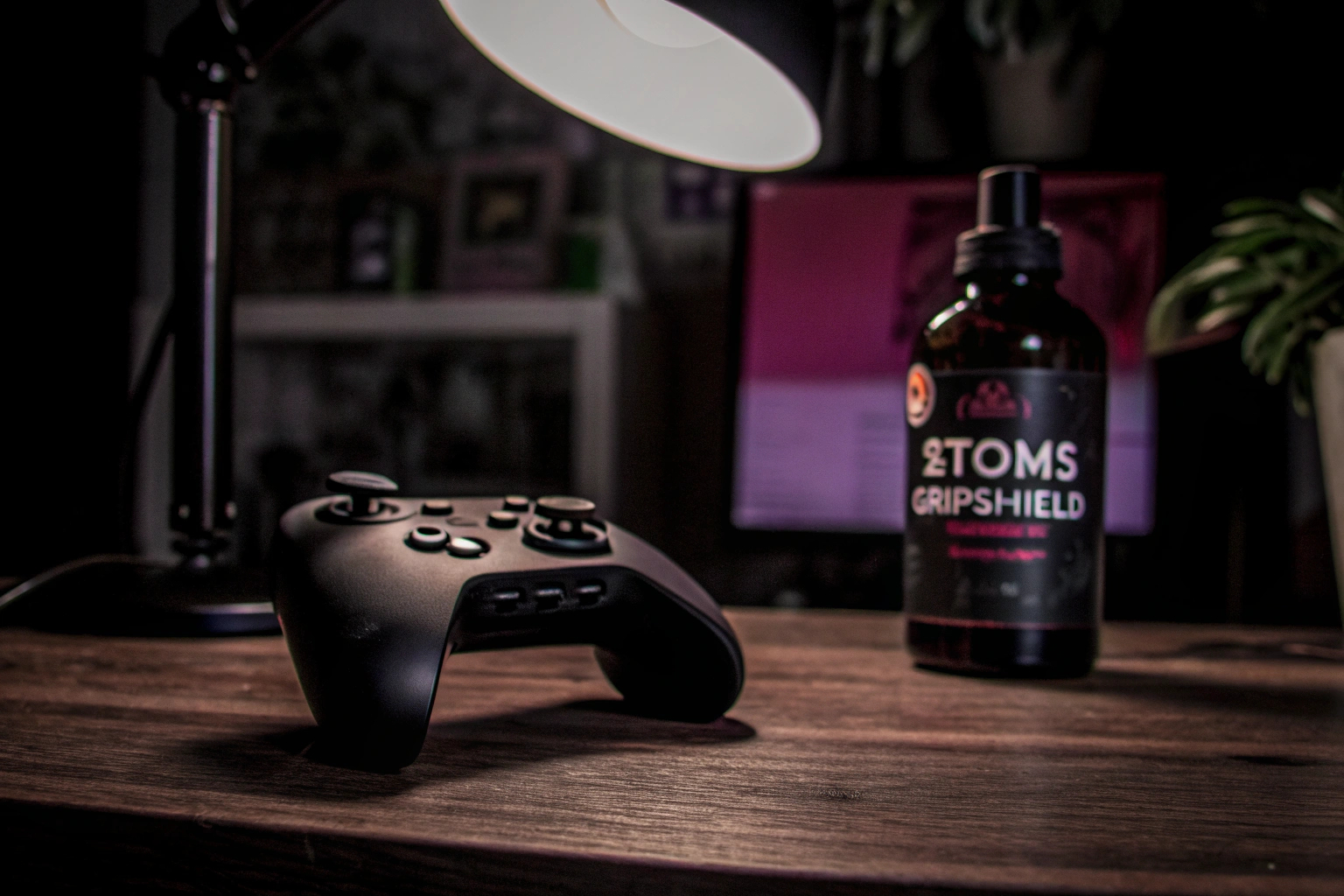 Eine Flasche 2Toms GripShield liegt neben einem Gaming-Controller auf einem Tisch. GripShield neben Gaming-Controller